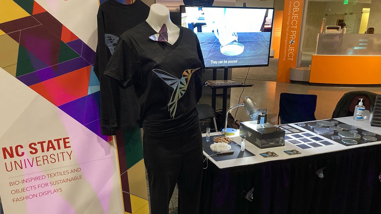 A table display showing a t-shirt with an iridescent hummingbird design - Bio-Inspired Textiles Promote Sustainable Fashion - College of Natural Resources News - NC State University