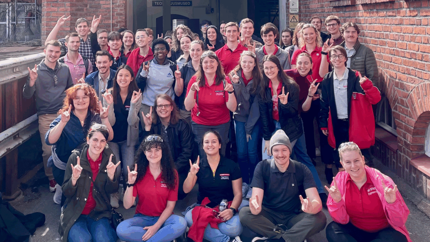 PIE trip attendees group photo holding up wolfies - Paper International Experience - Forest Biomaterials at NC State University