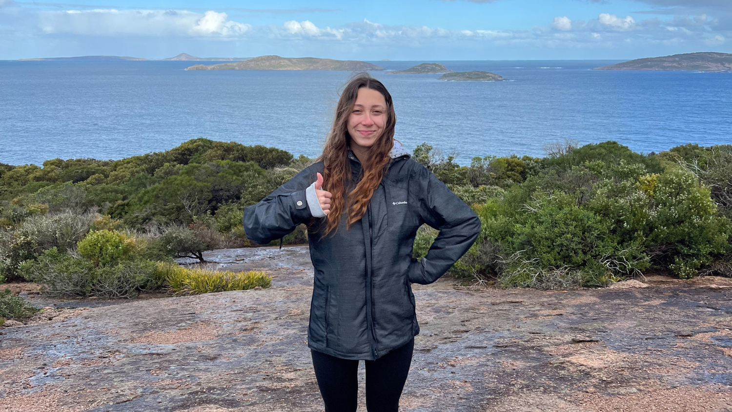 Tatiana standing on rocky and shrubby terrain with the ocean behind her- Tatiana Frontera’s Semester in Australia - Forestry and Environmental Resources at NC State University