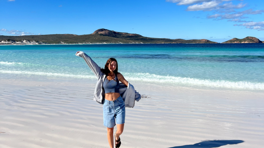 Tatiana standing on a white sand beach with mountains in the background - Tatiana Frontera’s Semester in Australia - Forestry and Environmental Resources at NC State University
