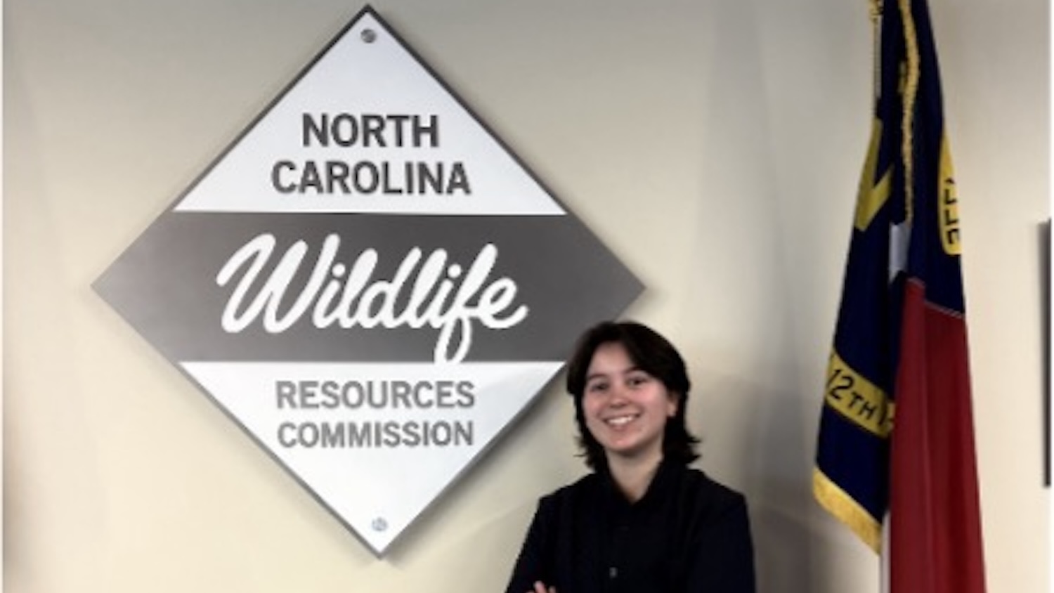 Jenna Birkevaag smiling next to the North Carolina Wildlife Resources Commission sign - Jenna Birkevaag: NCWRC - Managing People Not Wildlife - Forestry and Environmental Resources NC State University
