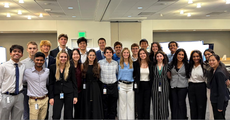 Group of professionally dressed young adults standing together indoors, smiling at the camera.