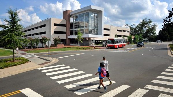 A photo of a Wolfline bus stopped at the West Parking Deck while students cross Varsity Drive at North Carolina State University