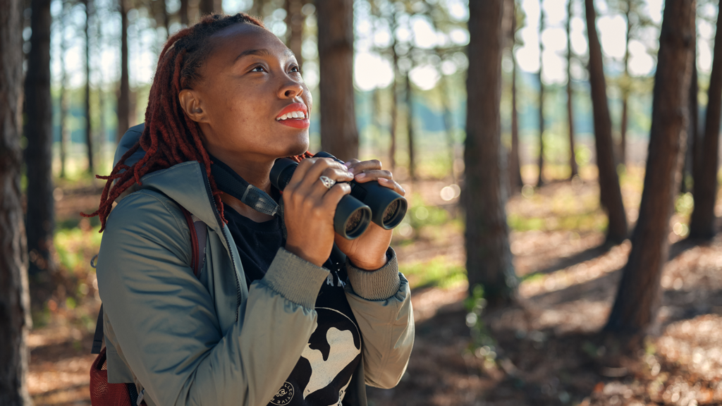 Ph.D. student Deja Perkins stands in a wooded area with binoculars