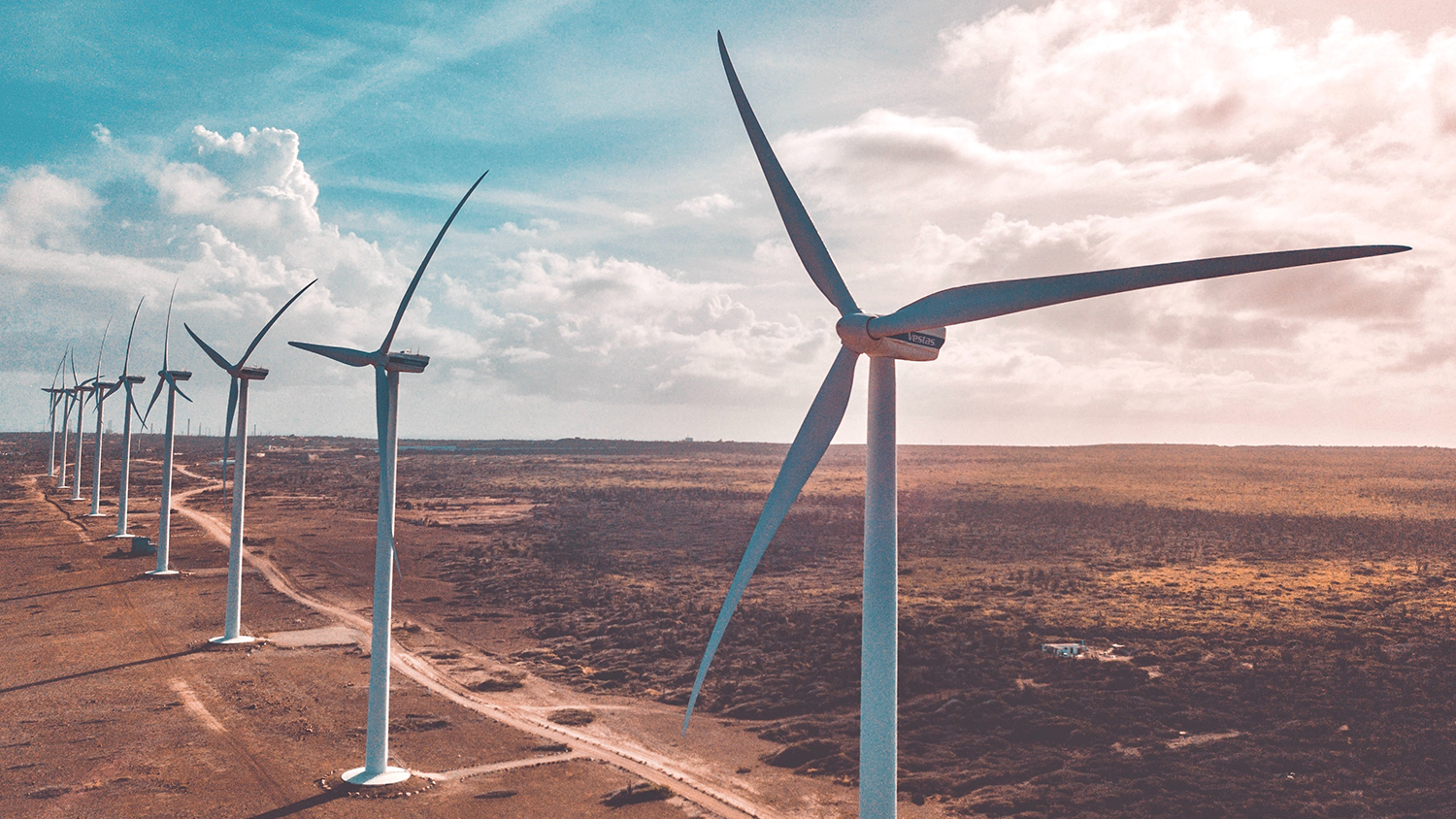 wind turbines in a row line a dirt road against a blue sky with white clouds