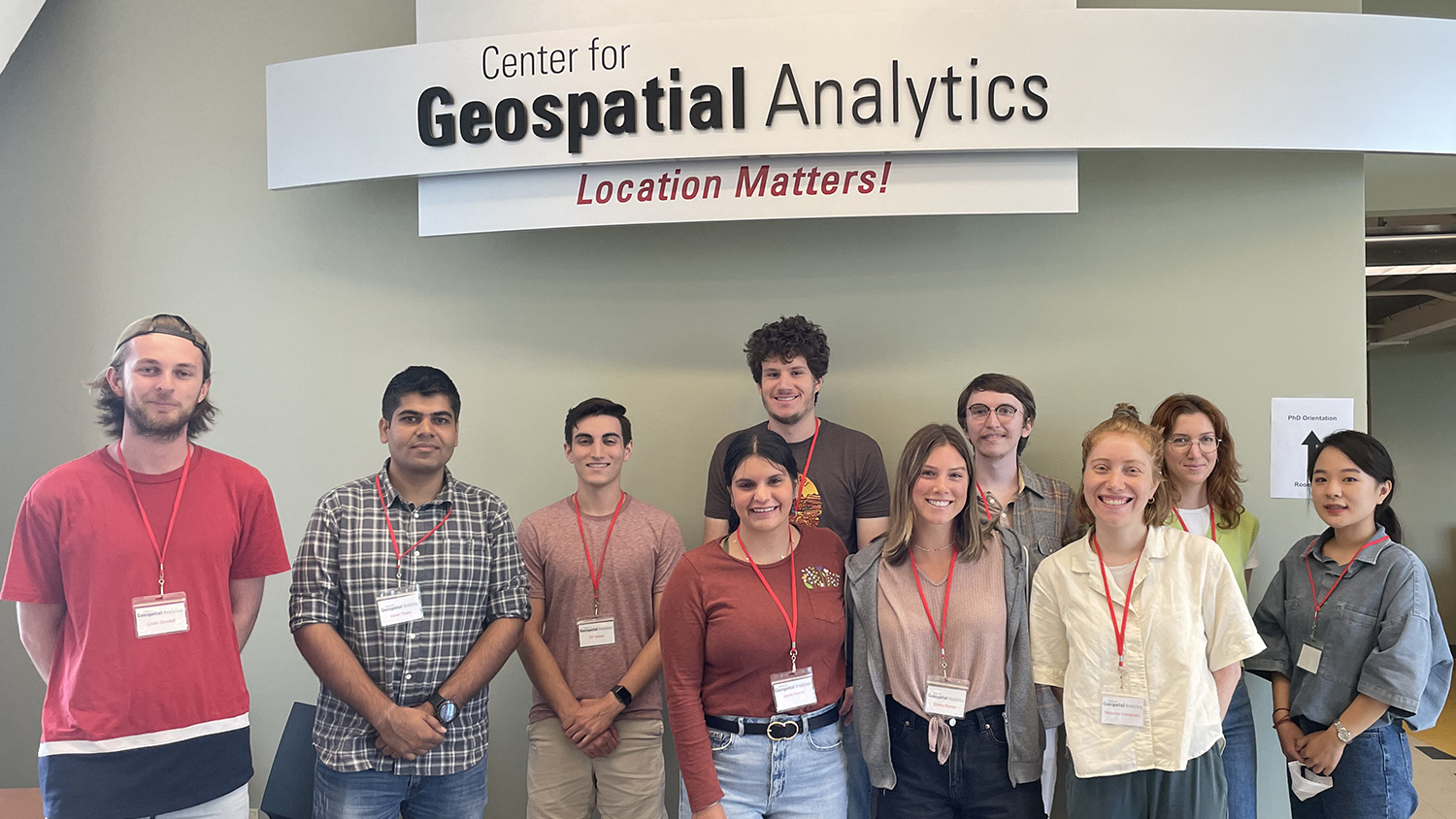 new Geospatial Analytics Ph.D. students stand under the Center for Geospatial Analytics sign at orientation