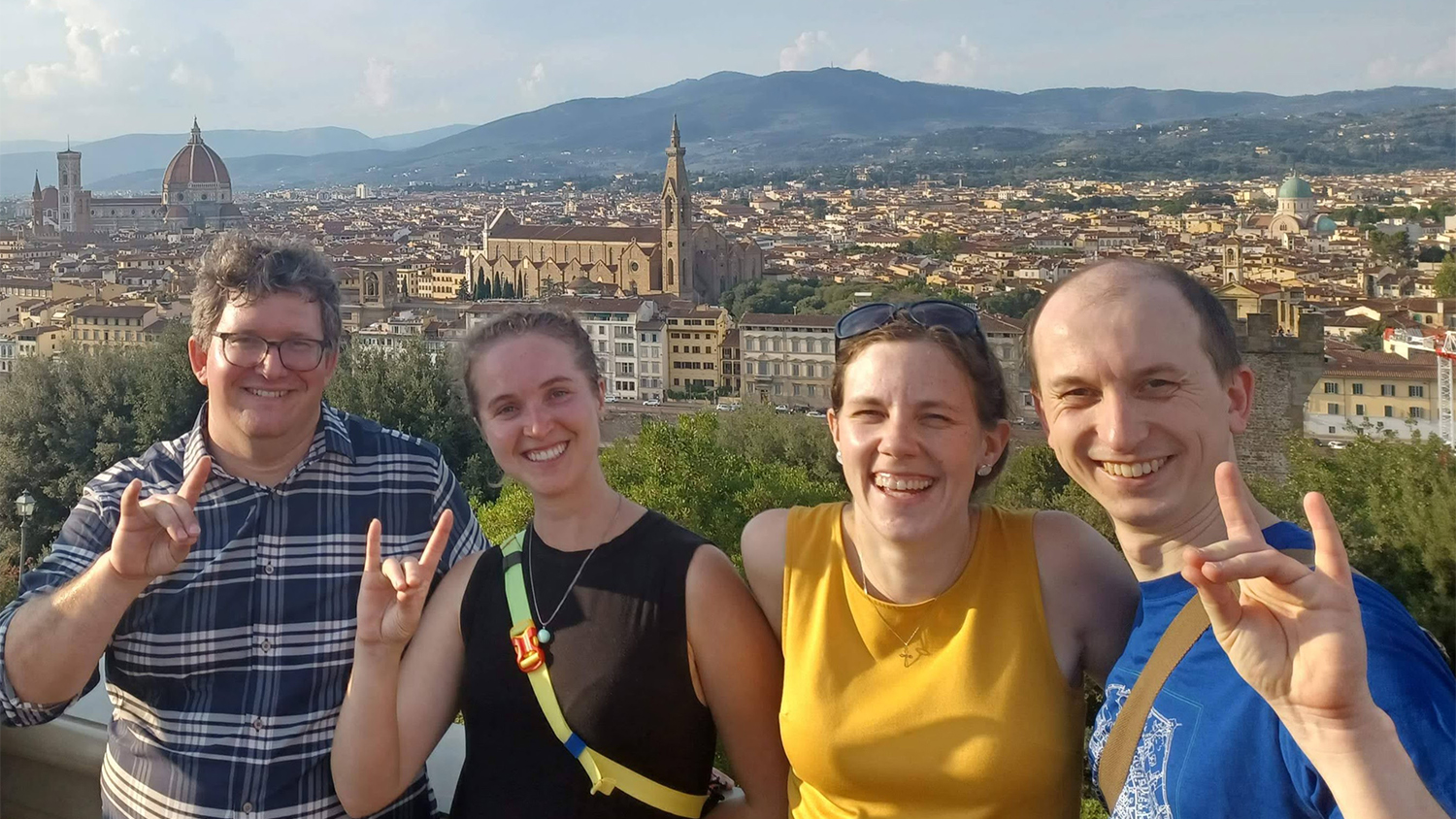 Four people give the Wolfpack hand sign with a cityscape of Florence, Italy behind them
