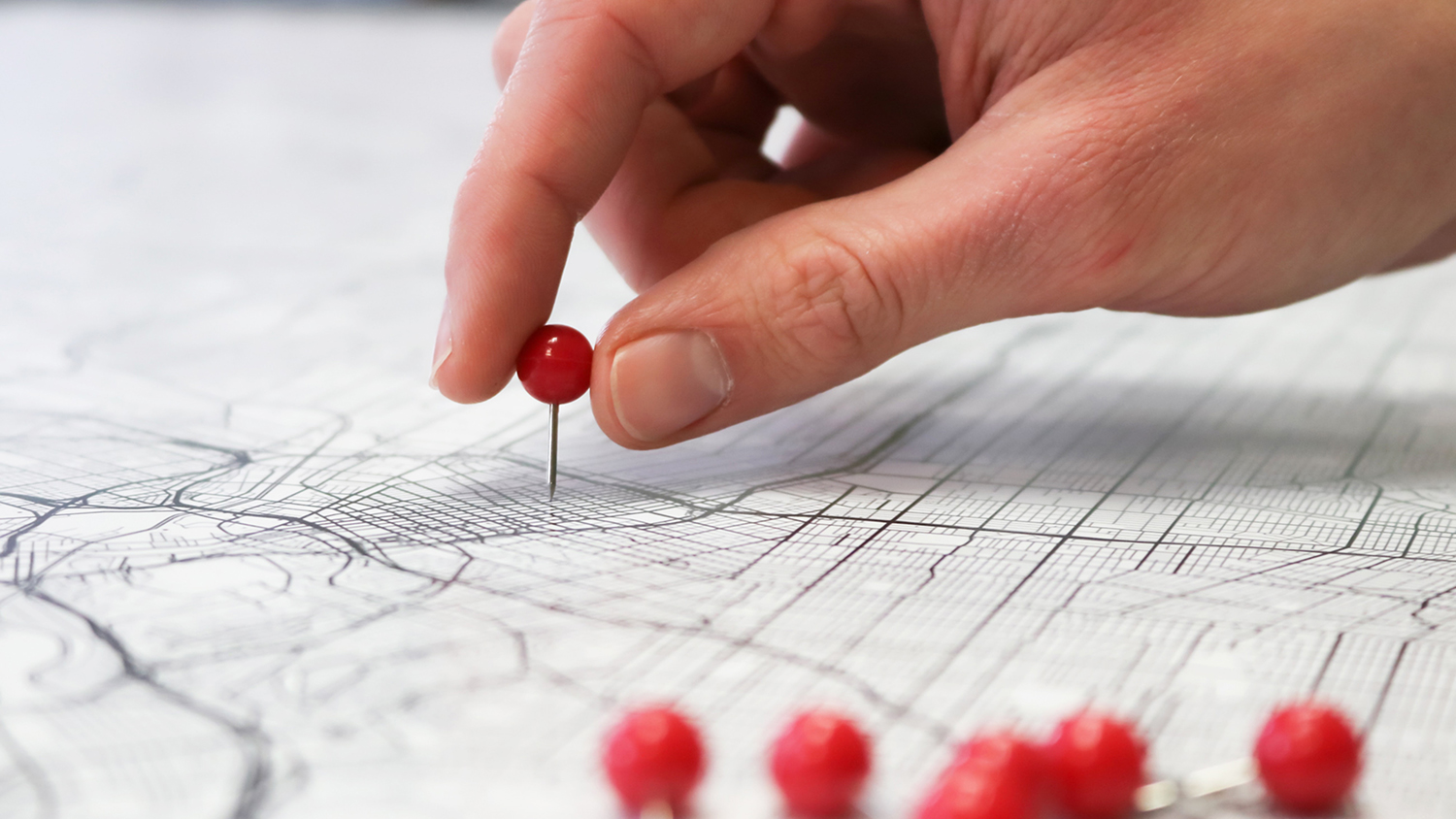 A hand places a red pushpin on a paper streetmap