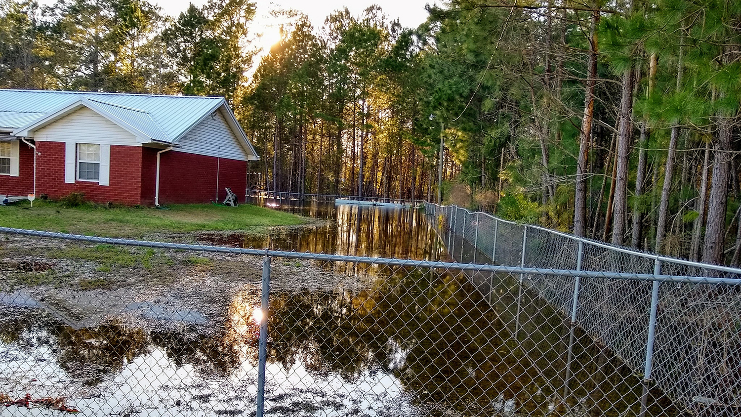 a red brick house is surrounded by flooding and a chainlink fence