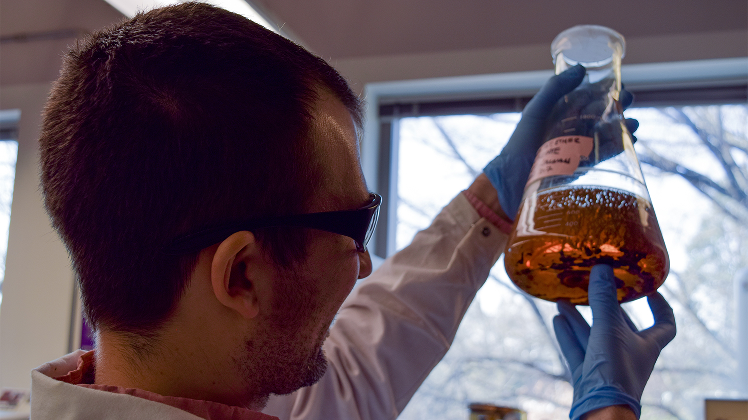 Matthew holds beaker in lab - Exploring Sustainable Air Travel With Jet Fuel From Trees - College of Natural Resources News NC State University
