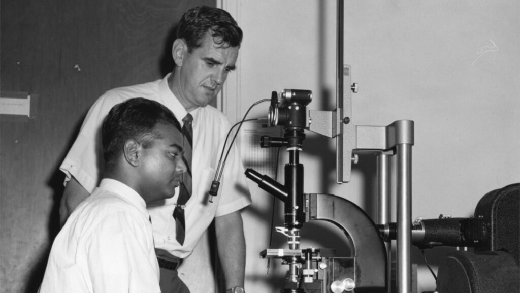 Ellwood stands next to student using microscope