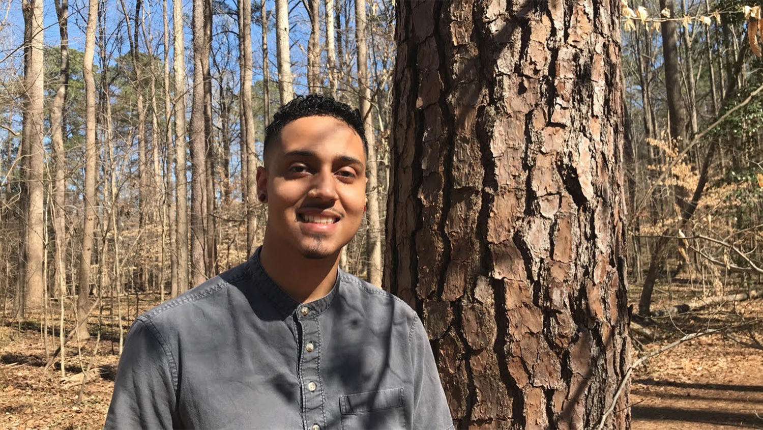 Norman poses and smiles in woods - Forestry Student Overcomes Challenges to Shine as Research Assistant - College of Natural Resources News NC State University