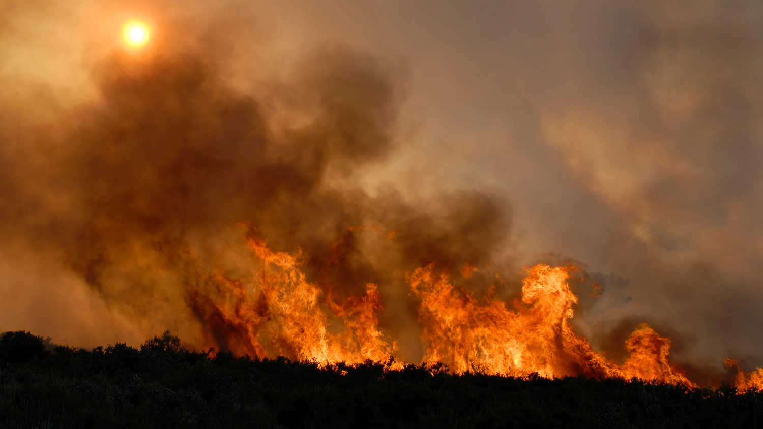 Wildfire emitting smoke along a mountain ridge.