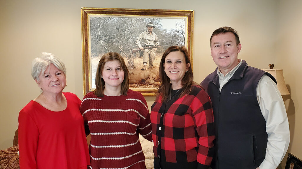 Dawn Mann and her family posing in front of a photo of Dr. Carroll L. Mann III. 
