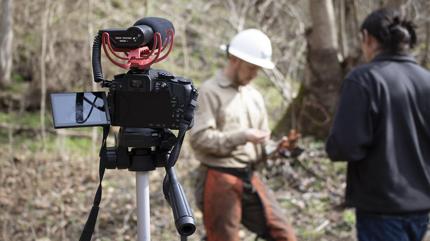 Two men talk in the background with a video camera on a tripod in the foreground - New Multimedia Story Map Shares Expweriences of Veterans in Fire Management - College of Natural Resources News NC State University