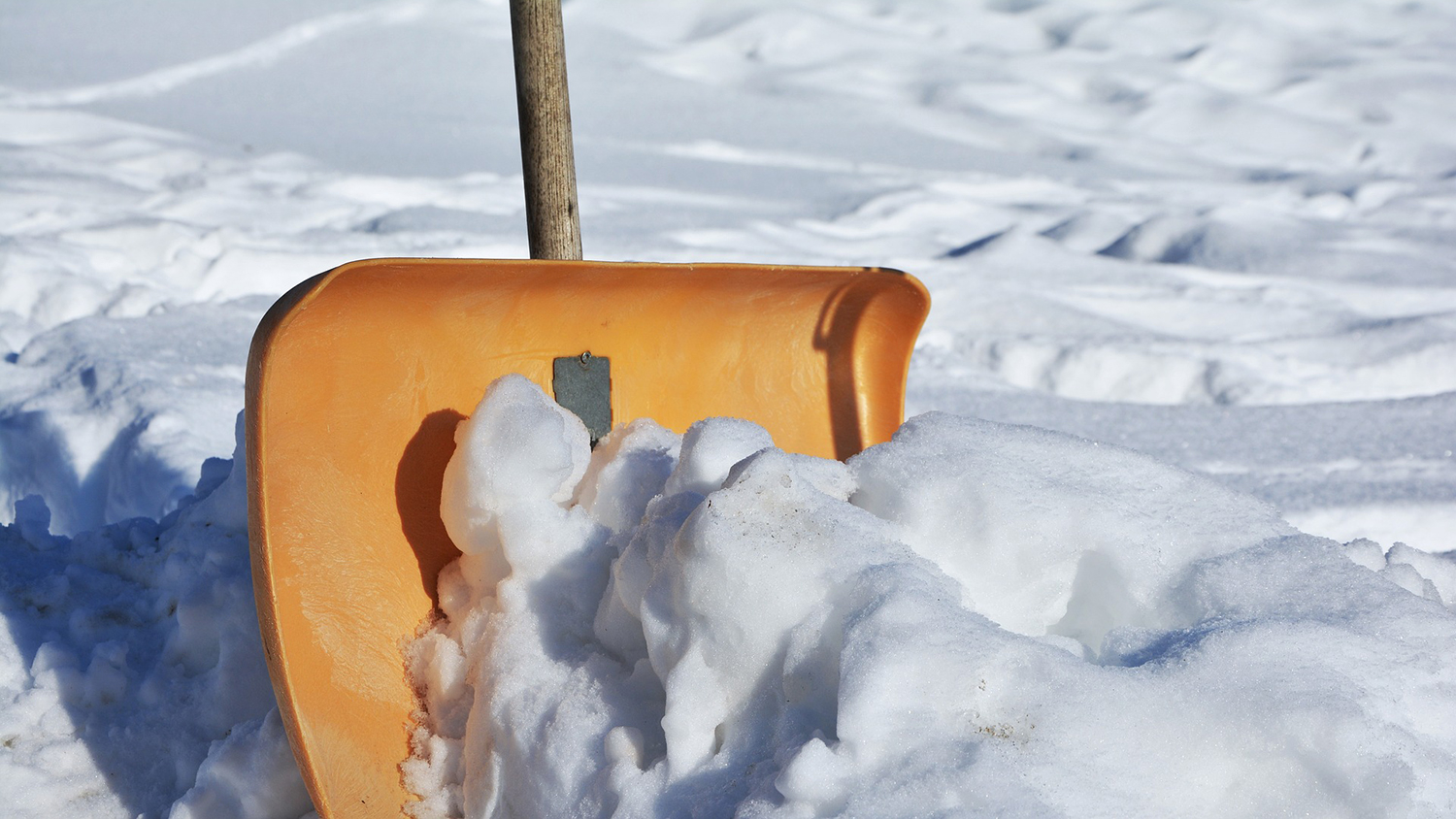 an orange snow shovel cuts through a pile of snow