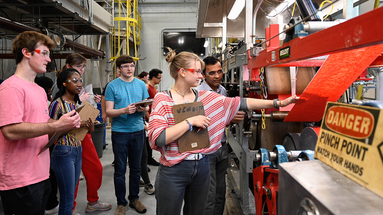 NC State students examine the “Wolfpack Baby” fourdrinier, a machine used for the evaluation of a number of furnishes and process conditions for papermaking.