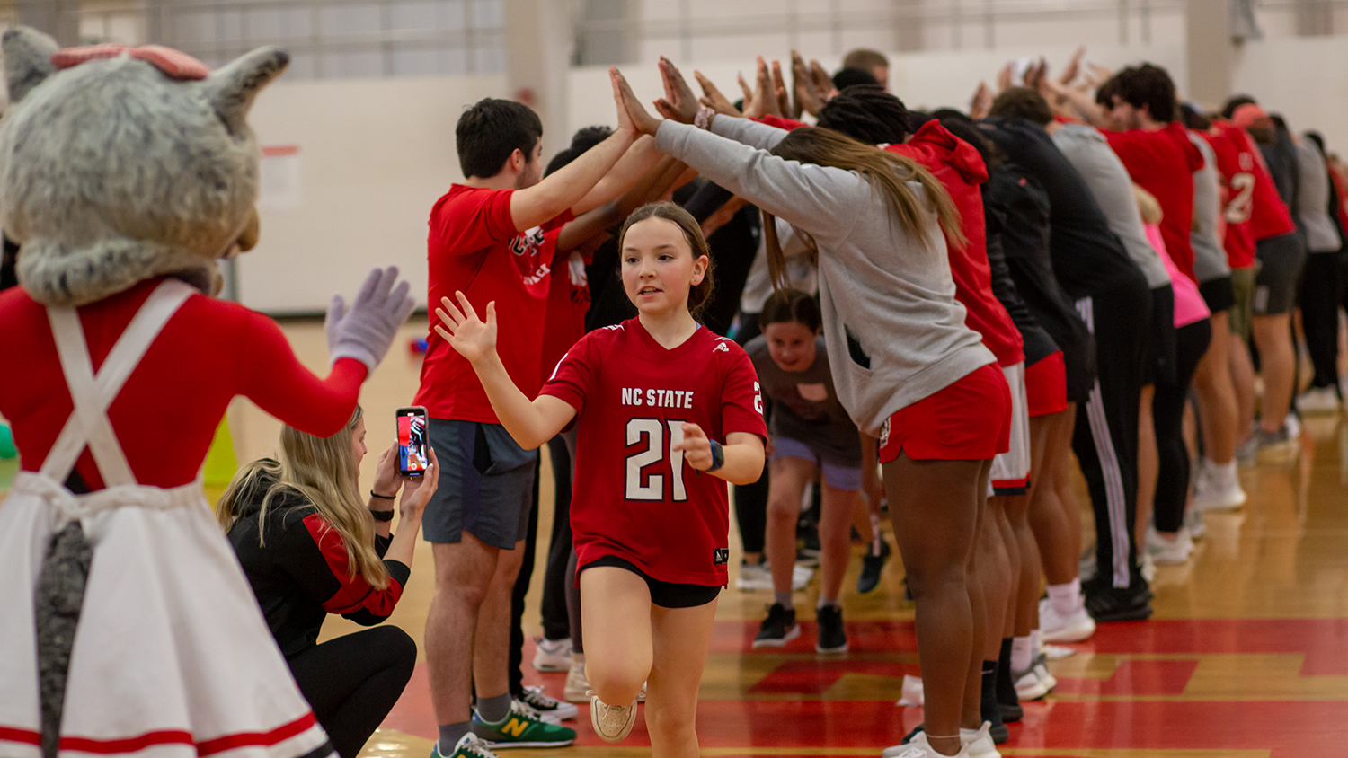 Girl high fives Ms. Wuf while running in Carmichael Gym - NC State Hosts Clinic to Promote Equity for Girls and Women in Sports - College of Natural Resources News NC State University
