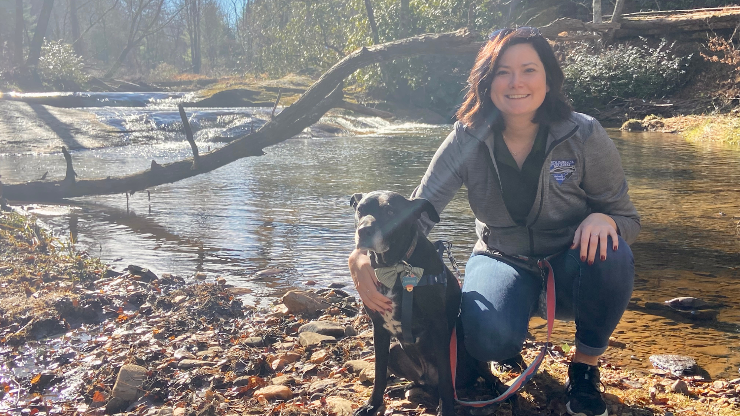 Kat stoops by creek with her dog - Graduation to Vocation: Kat Deutsch is Developing State Park Trails - College of Natural Resources News NC State University