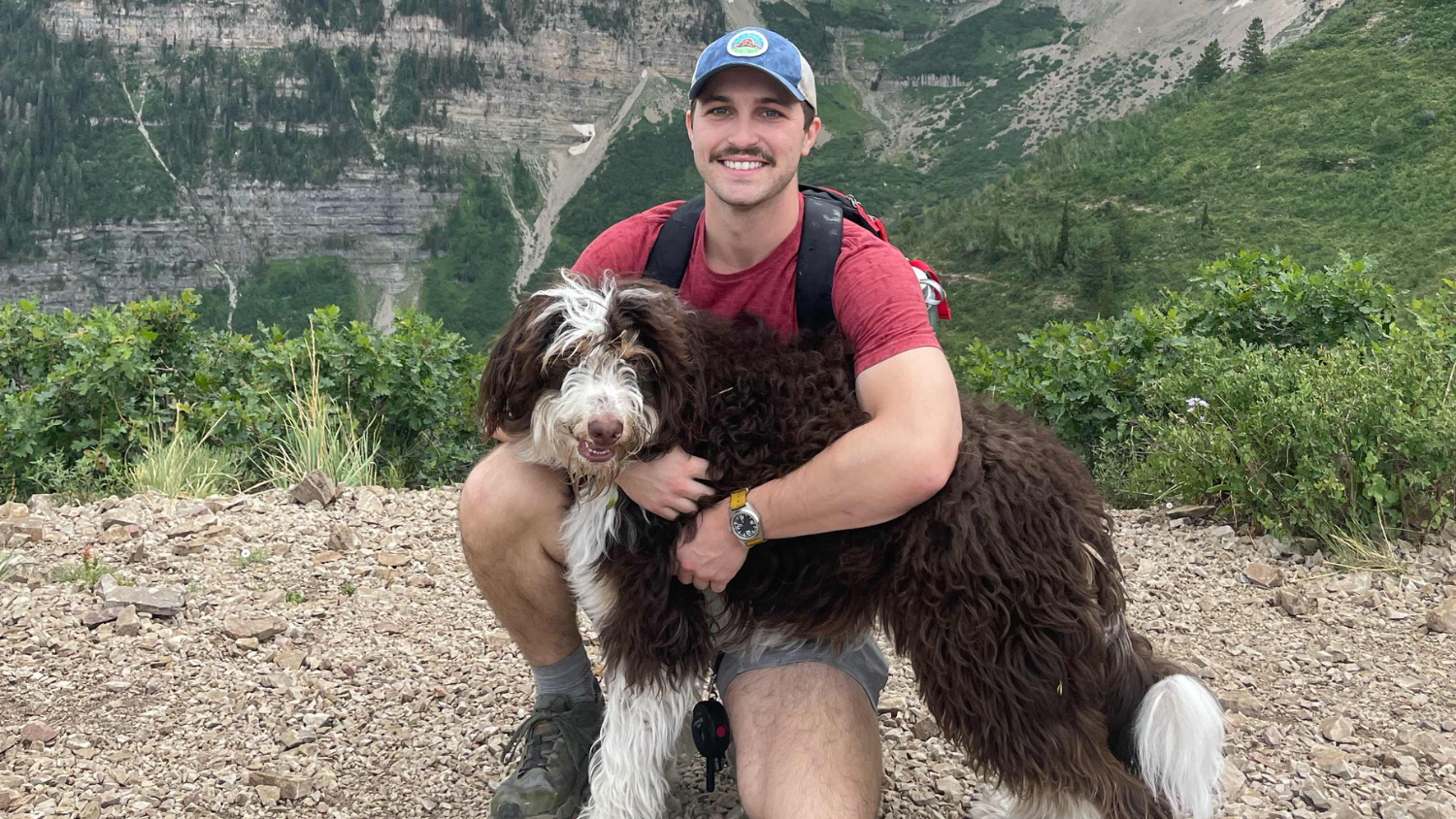 Joshua Lambert poses with his dog in front of a mountain.