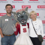 Two event event attendees pose with Mrs. Wuf