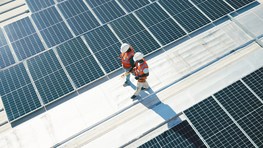 Two maintenance worker walking on a roof with solar panels.