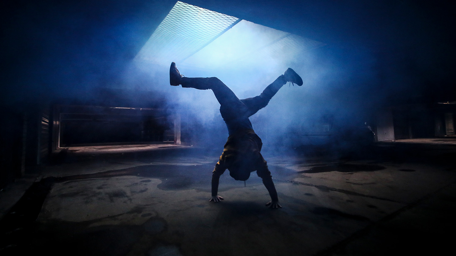 Silhouette of a person breakdancing in an underground garage.