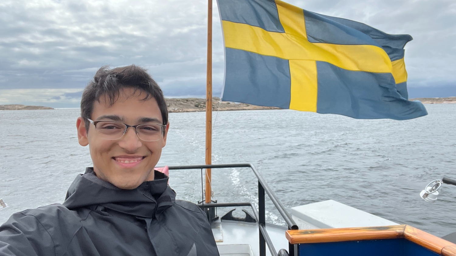 Matthew Menon posing for a photo in front of the Swedish flag.