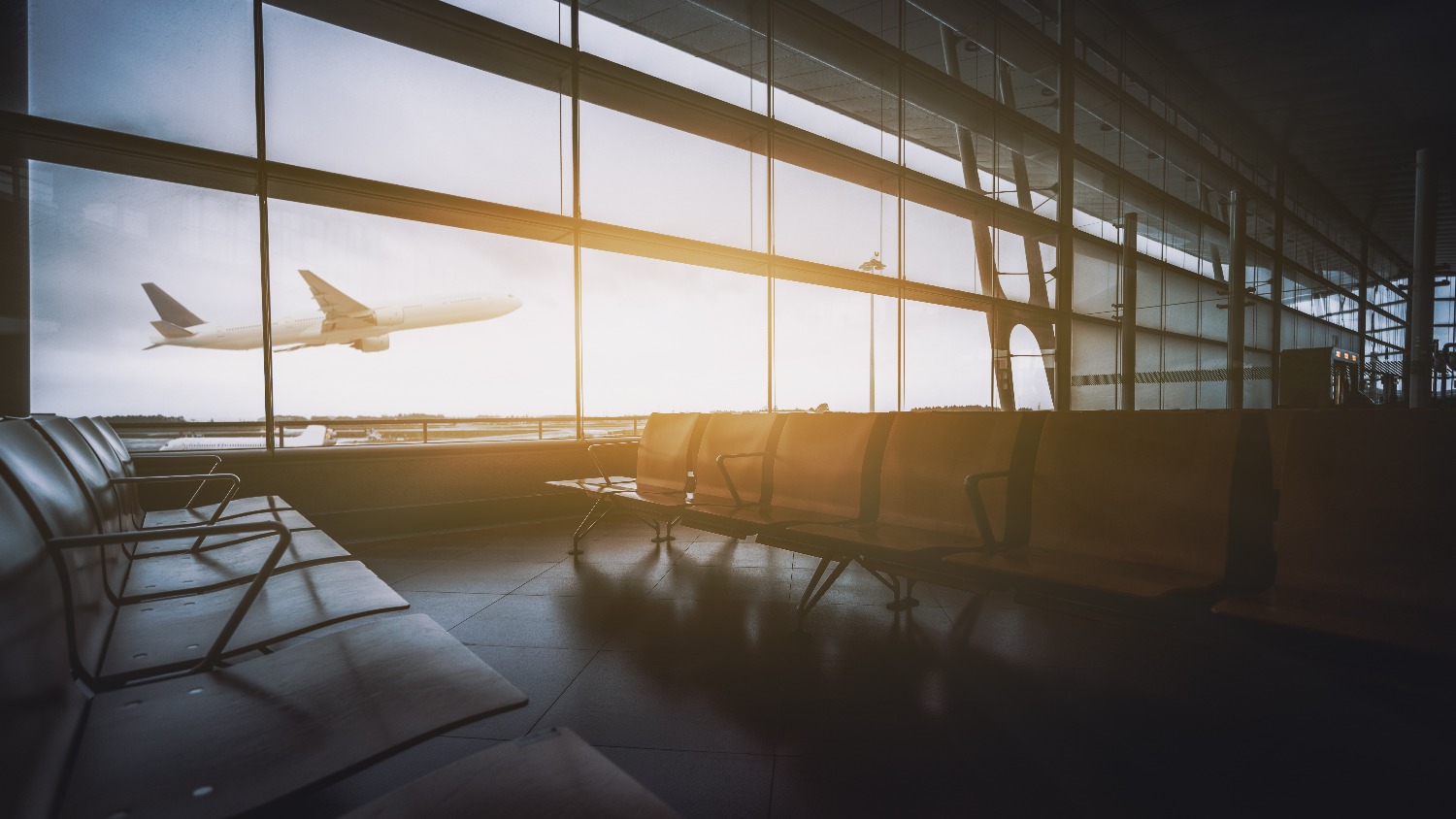 An empty airport terminal in the foreground, with an airplane taking off in the background.