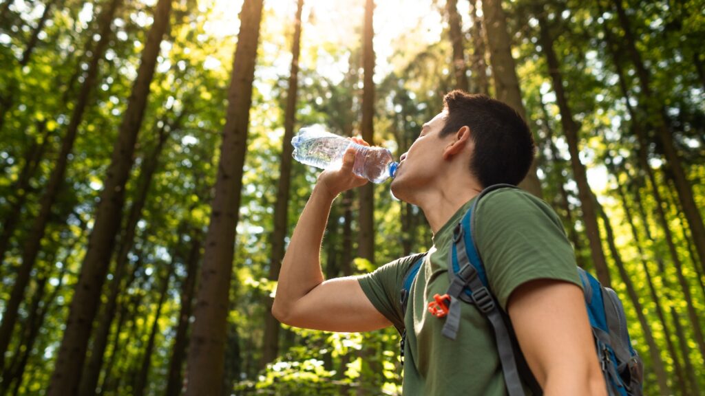 Man drinking bottle of water while hiking through the forest.