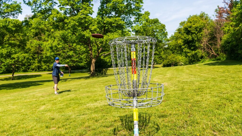 Man throwing a red, plastic disc at chain basket.