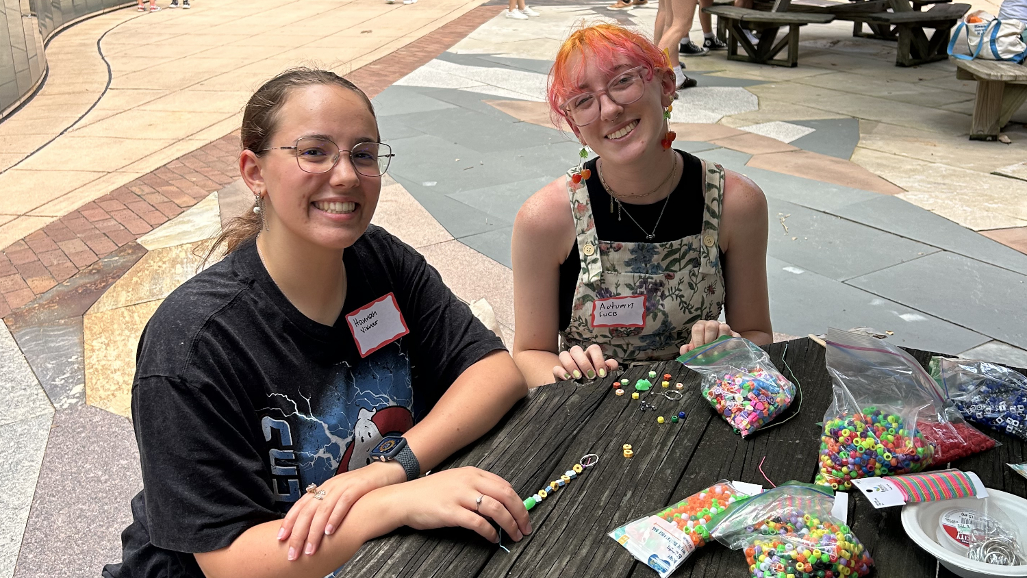 Two students smile as they make bead bracelets at a picnic table. - Admissions - College of Natural Resources at NC State