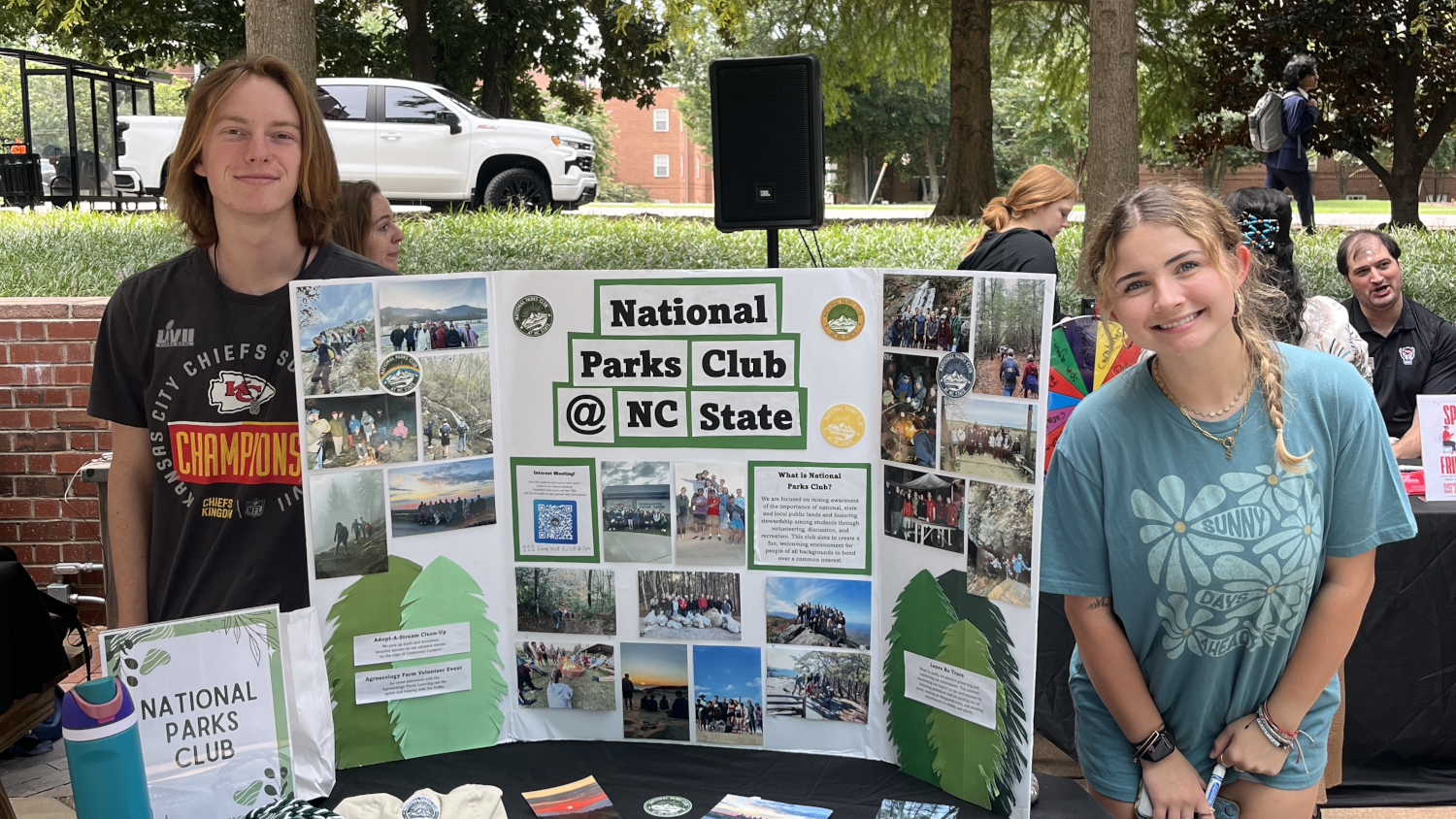 Two students smile with their club poster 