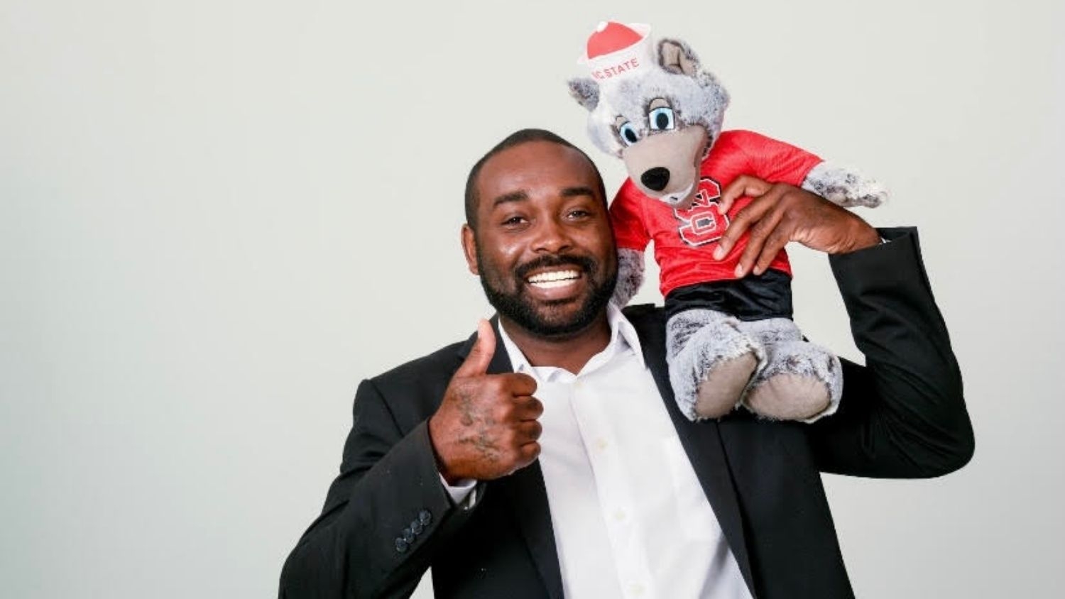 Rashawn King giving thumbs-up with NC State wolf stuffed animal on shoulder